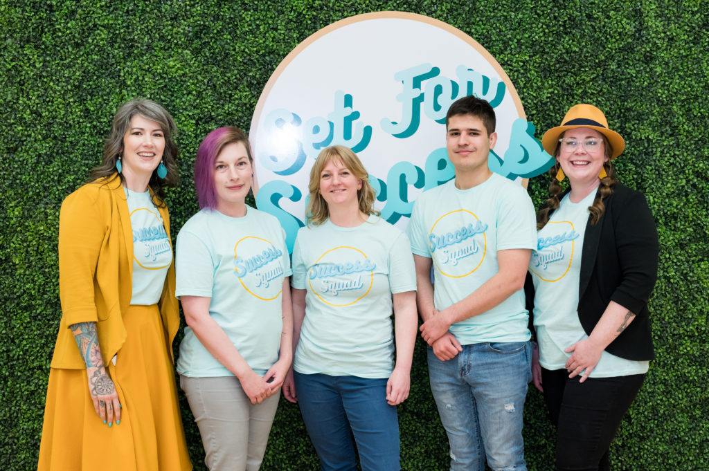 Four women and one man stand together with matching shirts that say Success Squad against a greenery wall with the Set For Success logo behind them